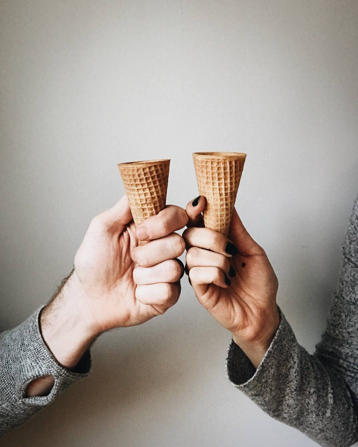 Two hands holding two ice cream cones.