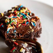 Brownie on a plate with rainbow sprinkles.
