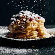 Powdered sugar being sprinkled on a stack of pancakes.
